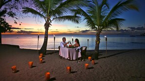 A beachside table set for two with a view of the ocean at sunset. - East Winds Saint Lucia (Gros Islet)
