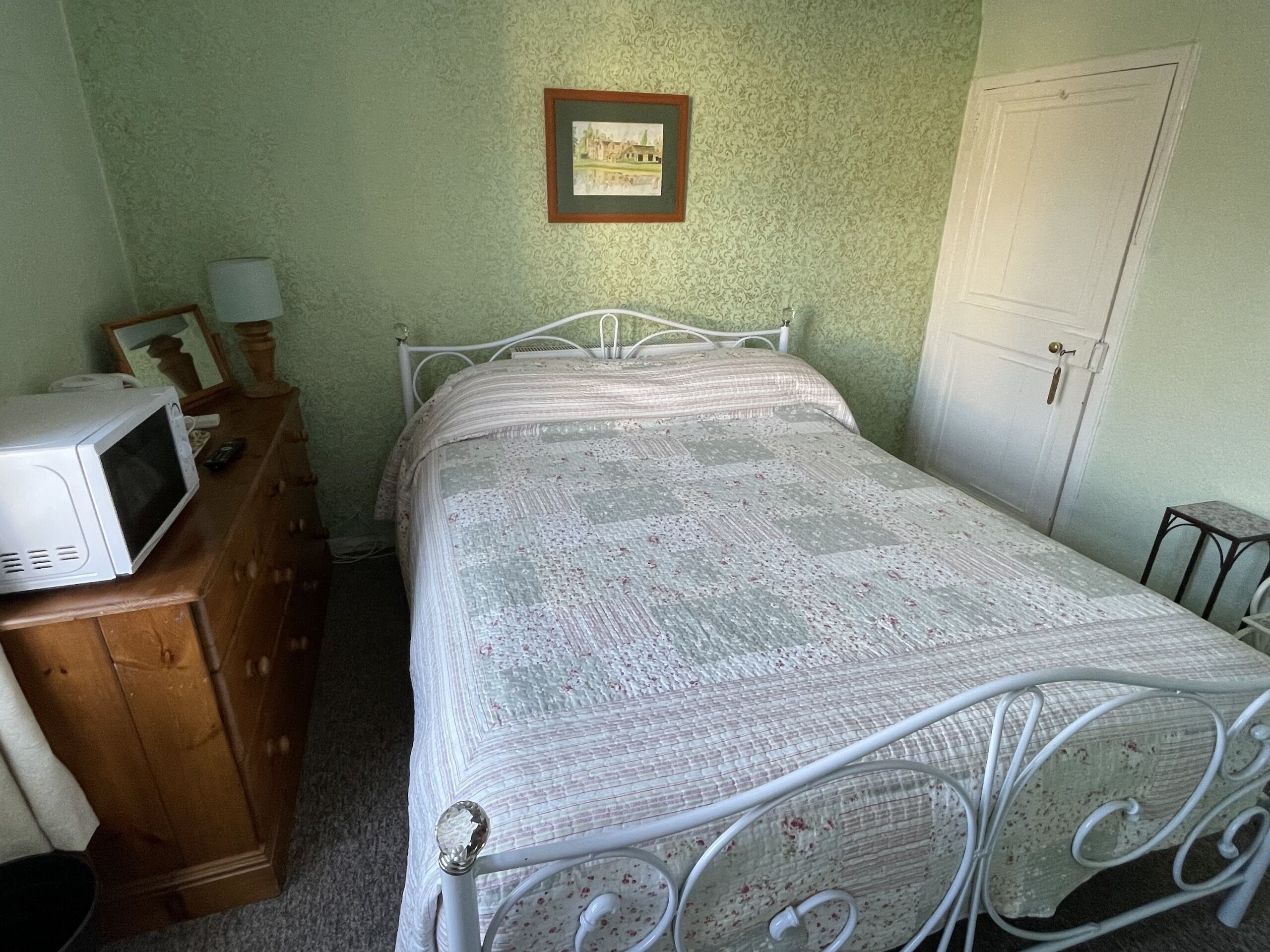Een slaapkamer met een bed, een dressoir, een magnetron en een ingelijst schilderij aan de muur.