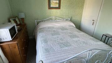 Een slaapkamer met een bed, een dressoir, een magnetron en een ingelijst schilderij aan de muur.