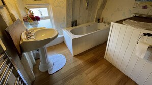 A bathroom with a sink, bathtub, wooden flooring, and a window with flowers. - The Bridge Street Historic Guest House (Sudbury)
