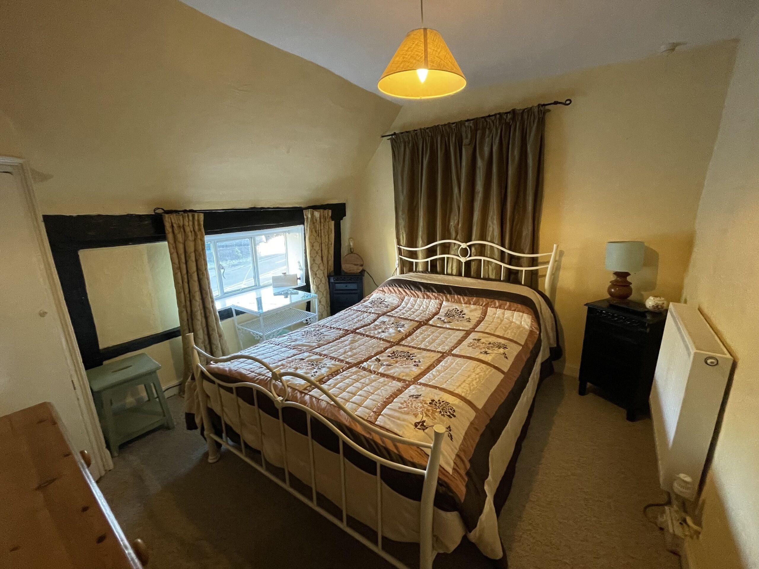 A bedroom with a bed, a bedside table, a lamp, a window with curtains, and a view of the outside.