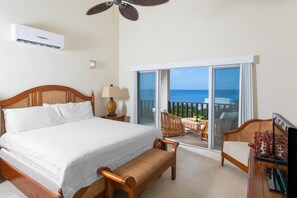 A hotel room with a large bed, a wooden bench, a TV, and a balcony with a view of the ocean. - Fountain Anguilla (Shoal Bay)
