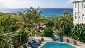 A pool area with lounge chairs, a view of the ocean, and lush greenery.