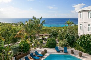 A pool area with lounge chairs, a view of the ocean, and lush greenery.