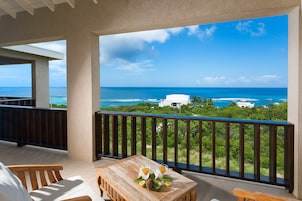 A balcony with a wooden table, two chairs, and a view of the ocean and greenery.