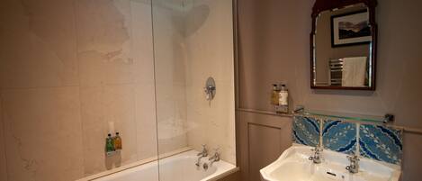 Casa de banho com chuveiro em cabine de vidro, banheira branca e lavatório com painel de azulejos decorativos.