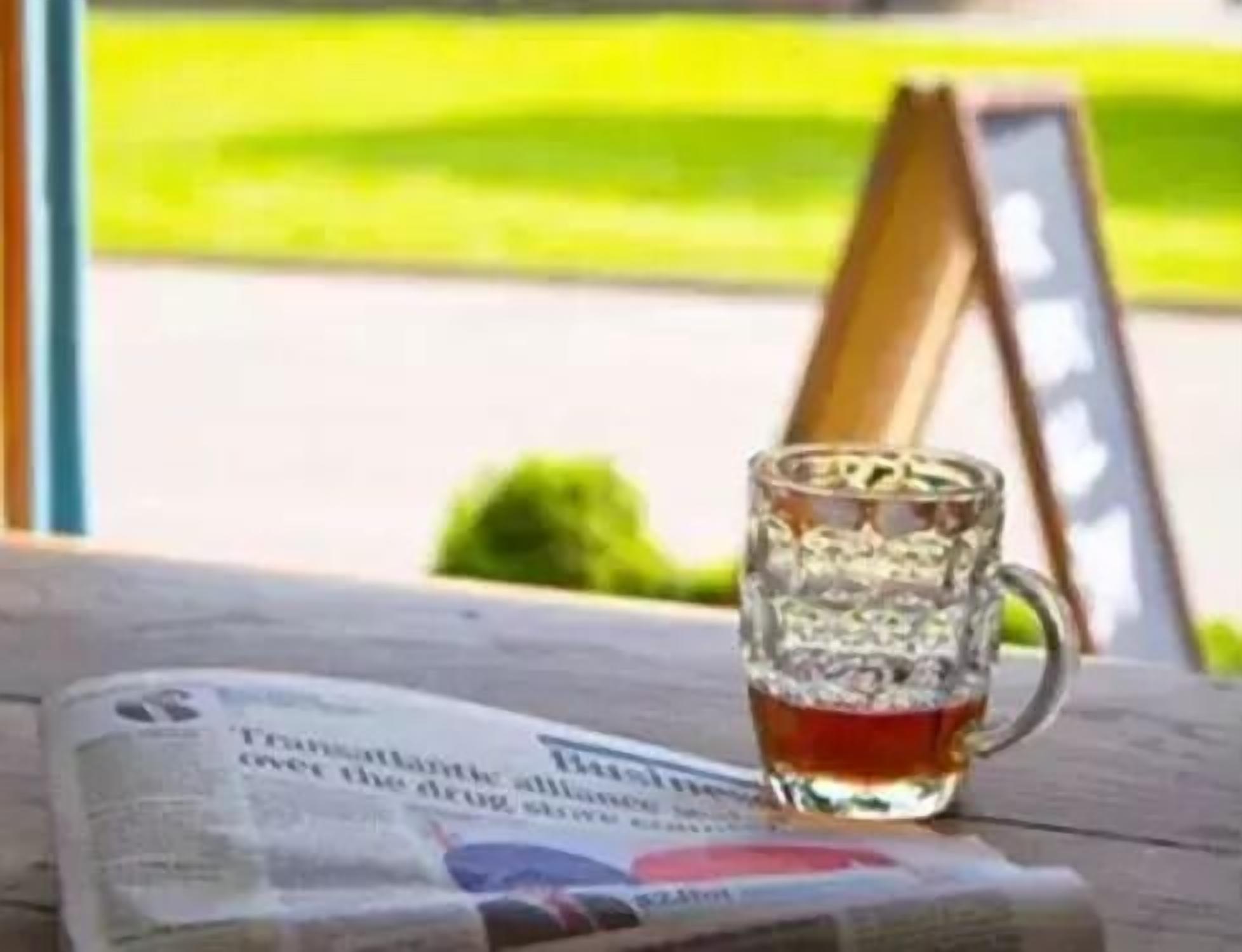 Un bicchiere di liquido ambrato su un tavolo di legno con un giornale.