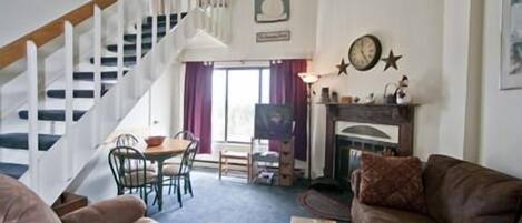 A living room with a staircase, a fireplace, and a dining area.