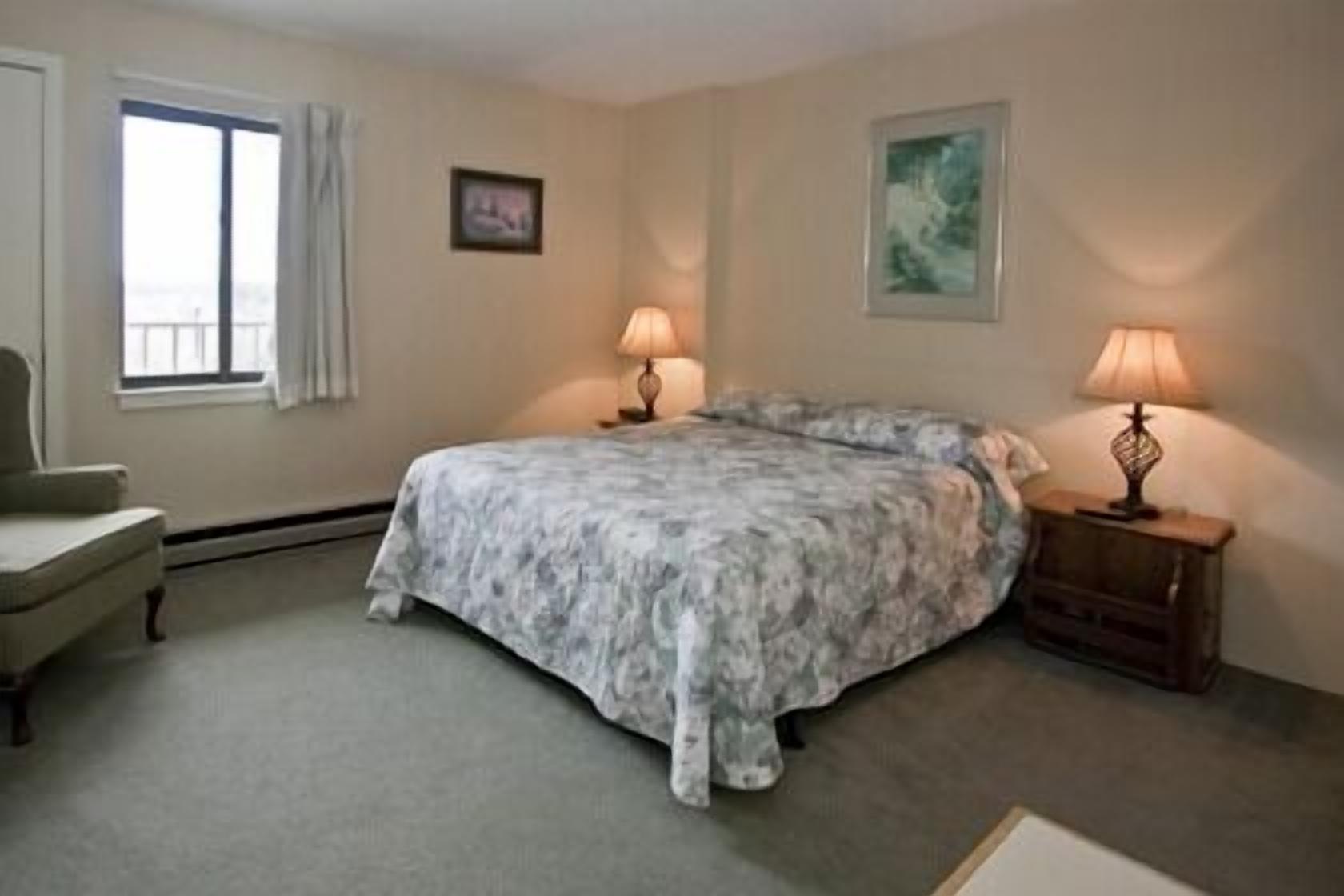 A bedroom with a bed, two bedside lamps, a chair, and a window.