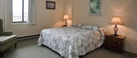 A bedroom with a bed, two bedside lamps, a chair, and a window.