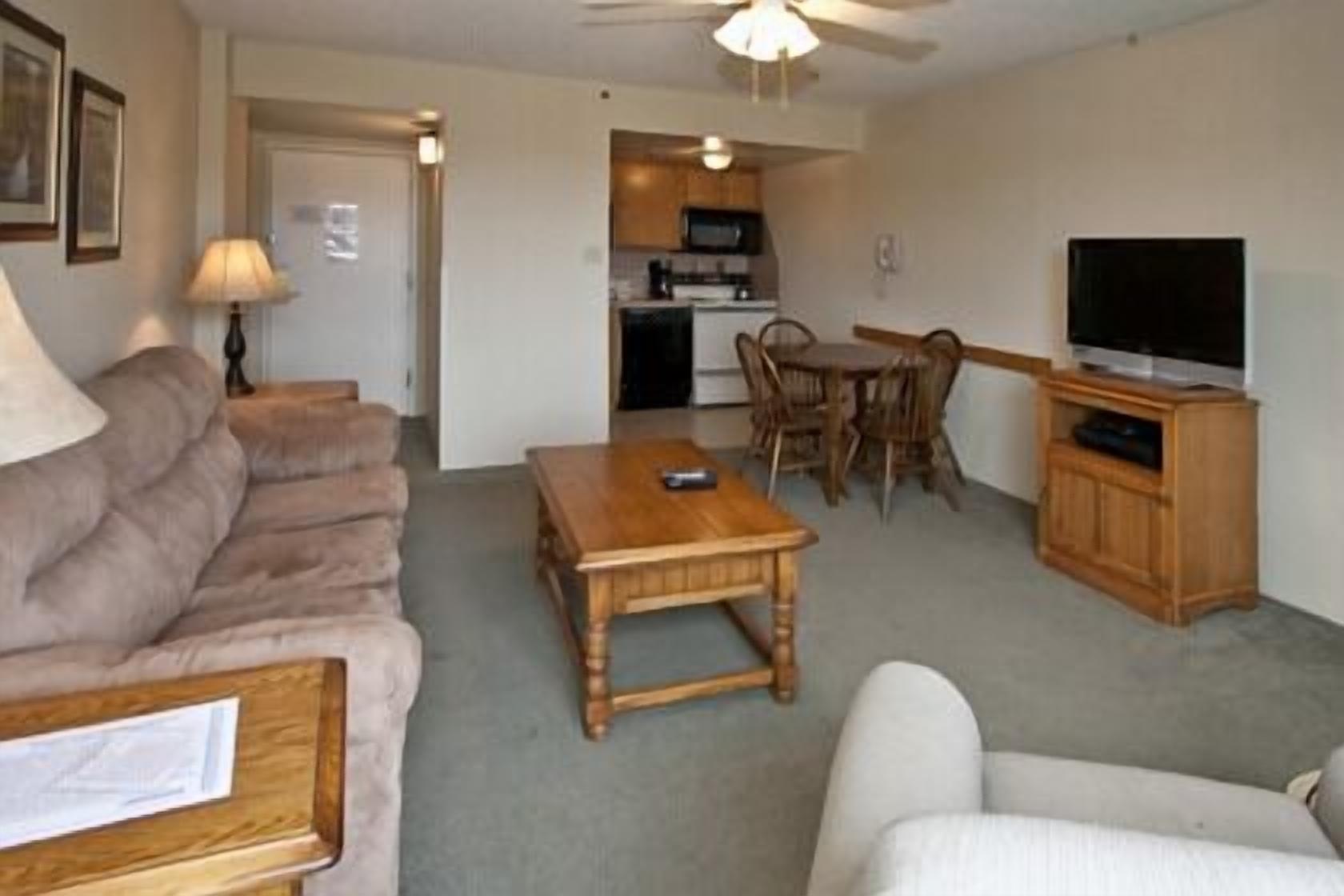 A living room with a sofa, a coffee table, a TV stand, and a dining area with chairs and a table.