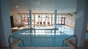 An indoor swimming pool with clear glass walls, a tiled floor, and several lounge chairs around the pool. - Silver Creek Lodge (Snowshoe)