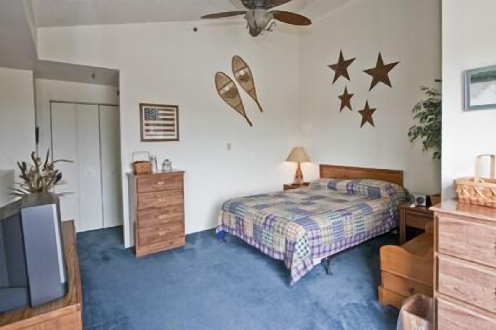 A bedroom with a bed, dresser, ceiling fan, wall decorations, and a door.