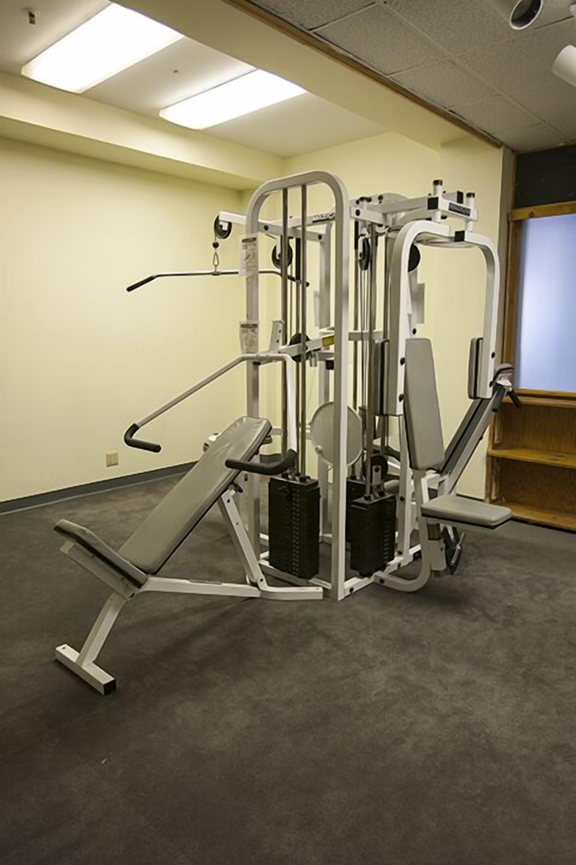 Une salle de sport équipée d’un banc de développé couché, d’une machine à presse à cuisses et d’autres appareils d’entraînement avec poids.