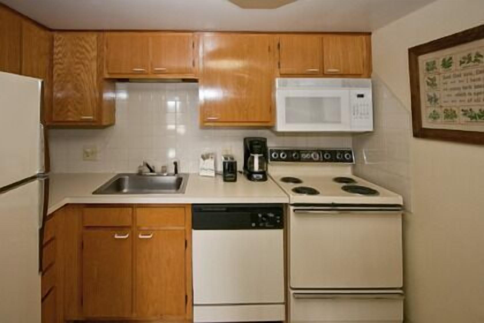 Une cuisine compacte avec des meubles en bois, un micro-ondes blanc, une cuisinière et un lave-vaisselle.