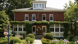A two-story brick house with a front porch, a small garden with flowers, and a mailbox. - B&B Au Virage (Magog)