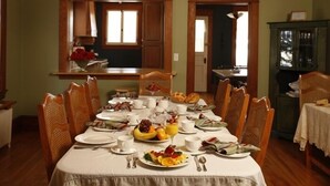A dining room with a long table set for breakfast, wooden chairs, and a green cabinet in the background. - B&B Au Virage (Magog)