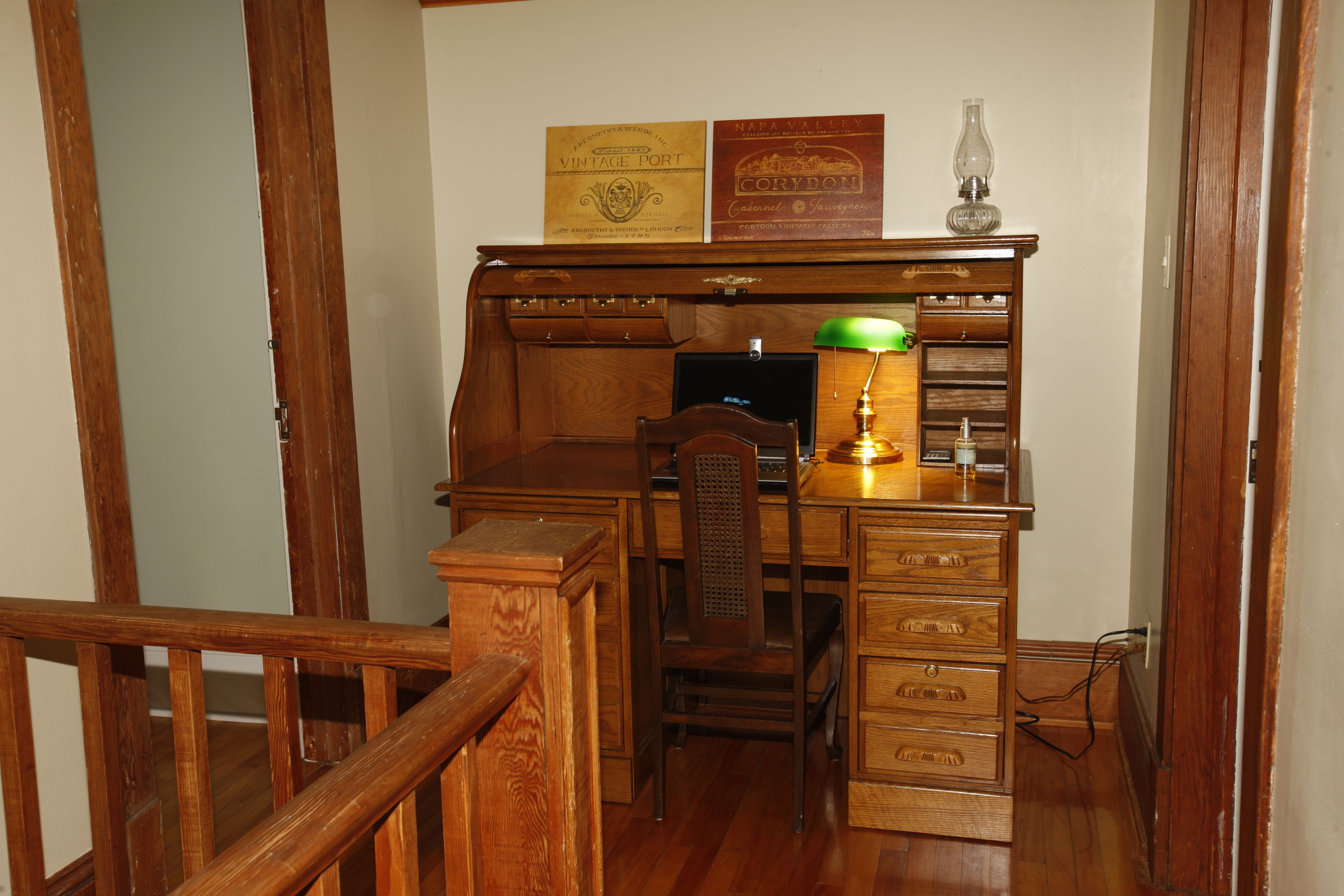 A wooden desk with drawers, a chair, and a lamp. There are two framed certificates on the wall above the desk.