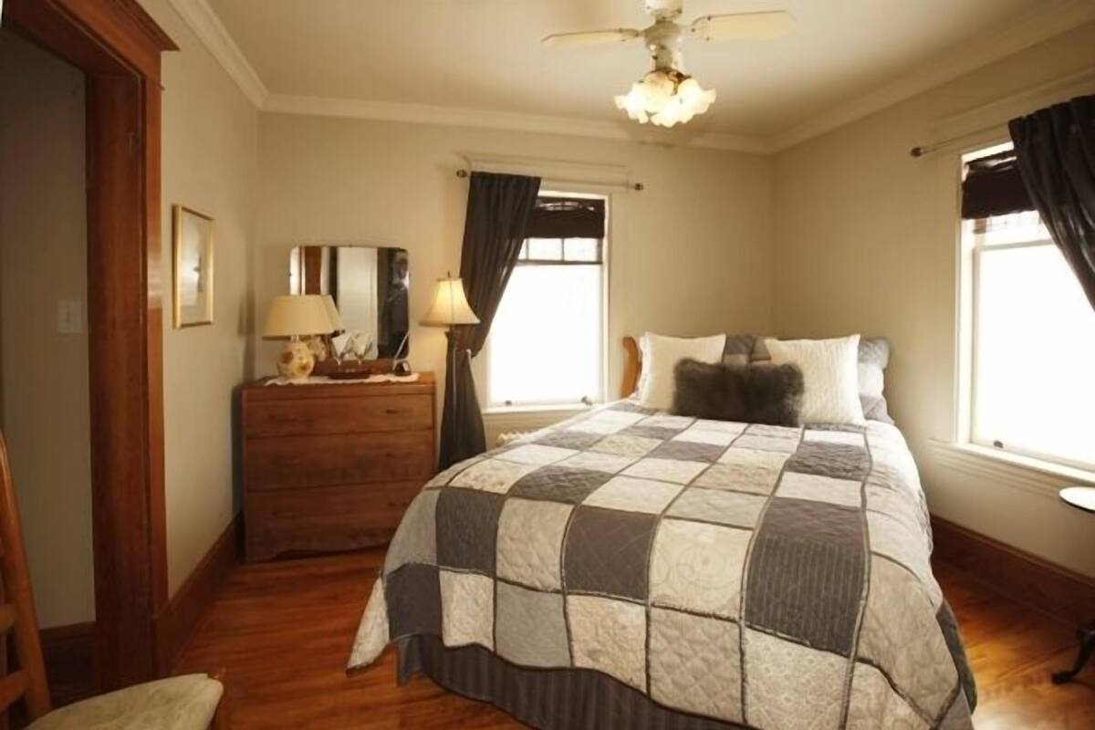 A bedroom with a large bed, wooden dresser, and a ceiling fan.