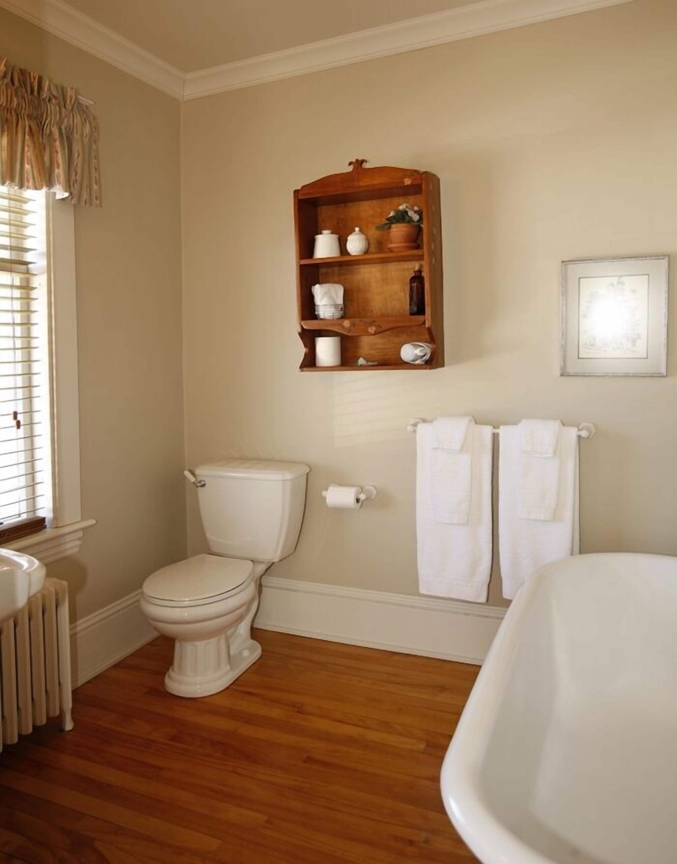 A bathroom with a toilet, a wooden shelf with kitchen items, a radiator, and a bathtub.