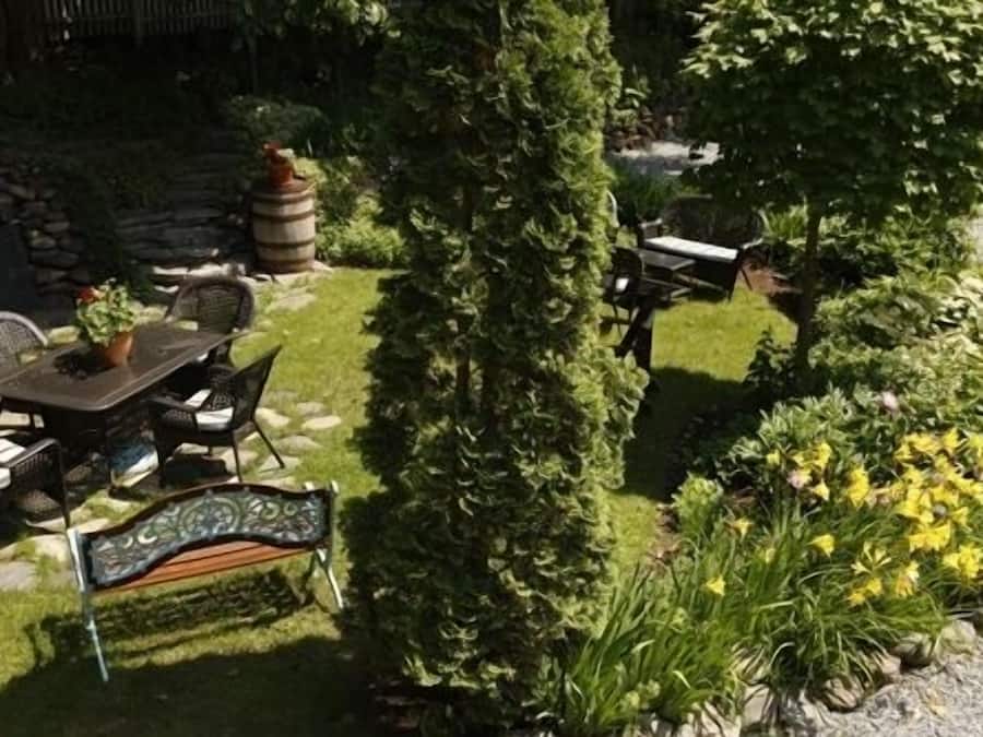 A garden with a table and chairs, a stone wall, and various plants.