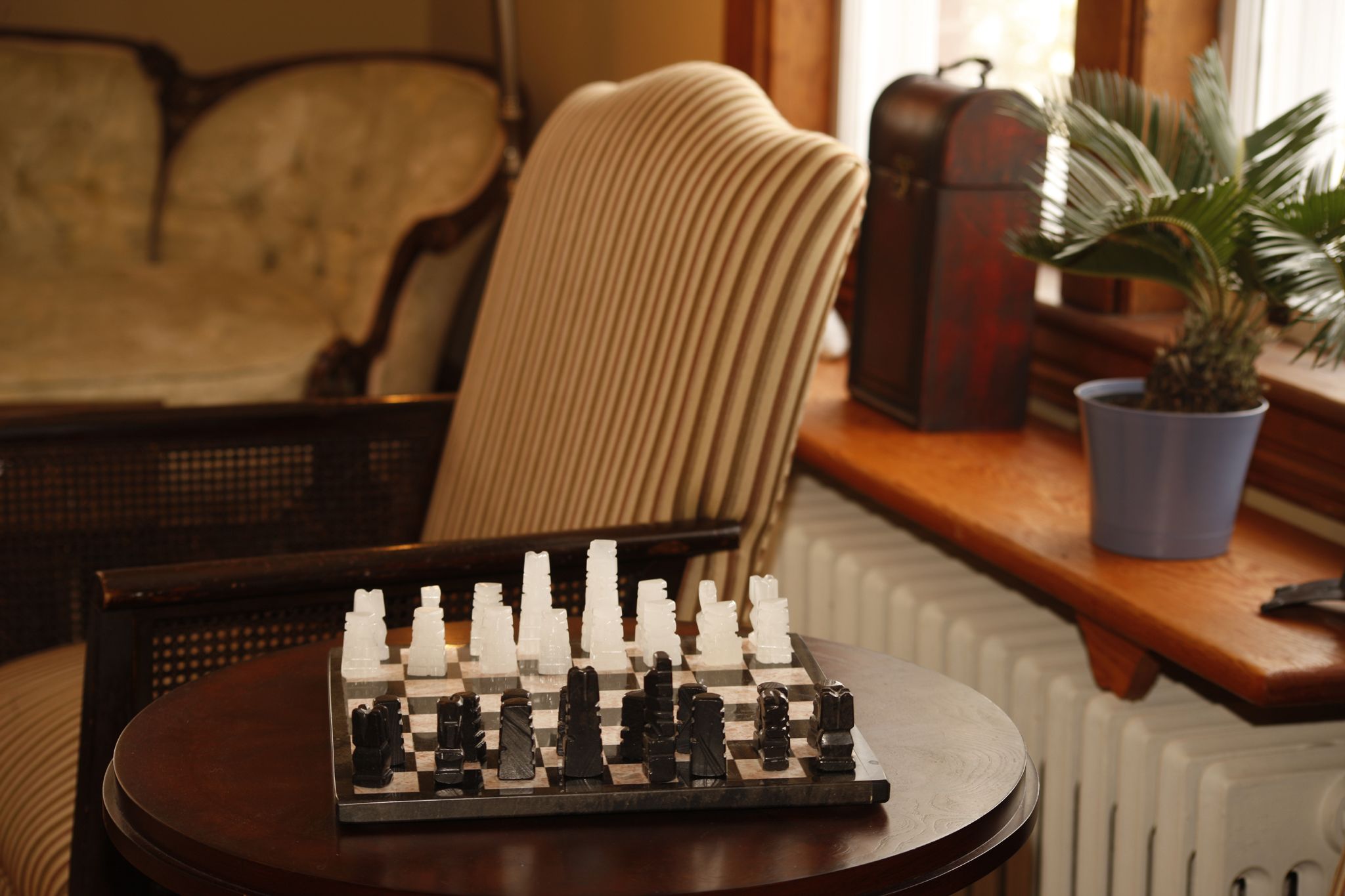 A chessboard on a table with a chair and a radiator in the background.
