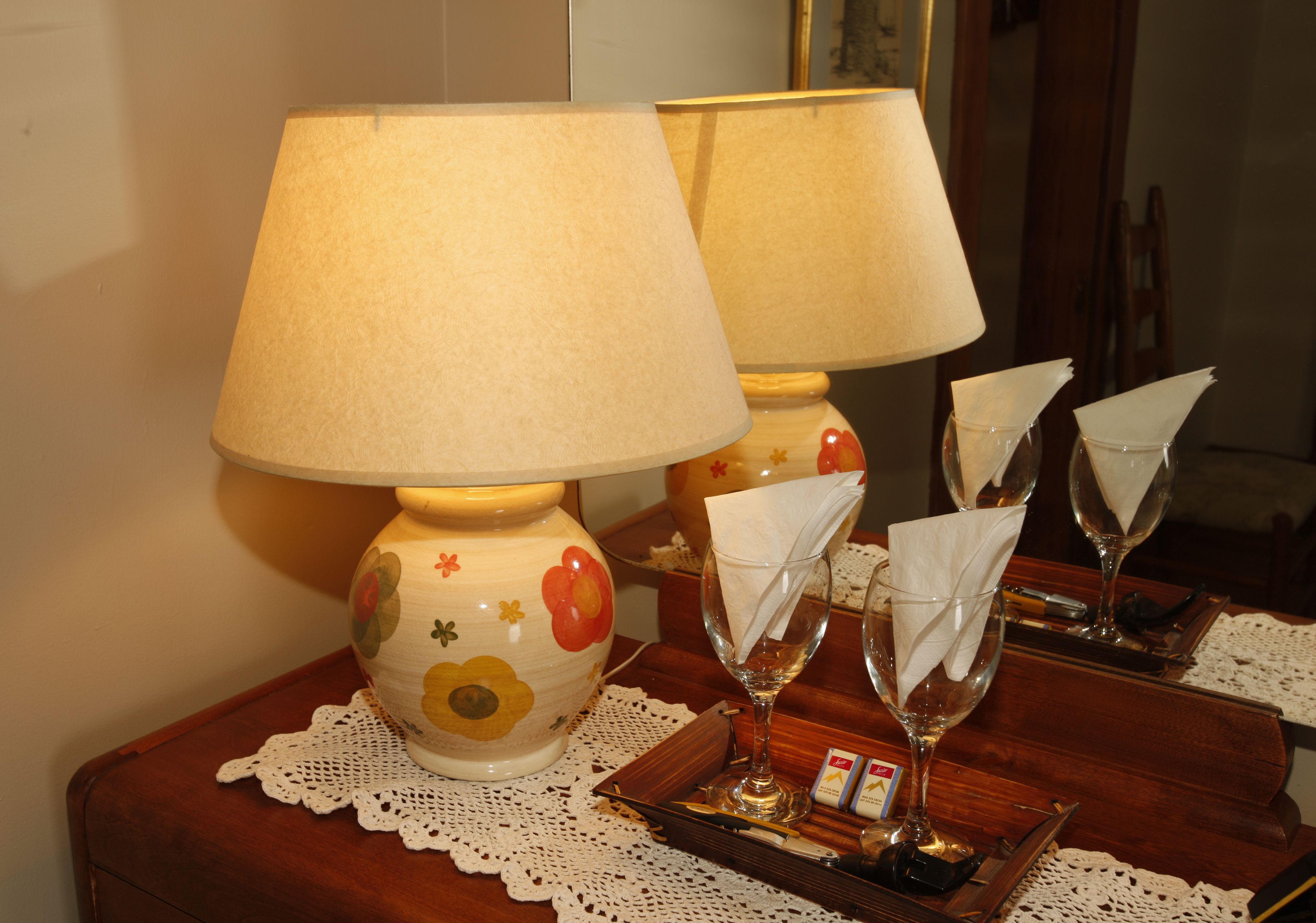 A table with a lamp, a vase with a floral design, and a tray with napkins and glasses.