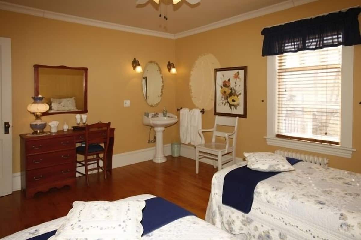 A bedroom with two beds, a dresser, a chair, a sink, and a window with blinds.
