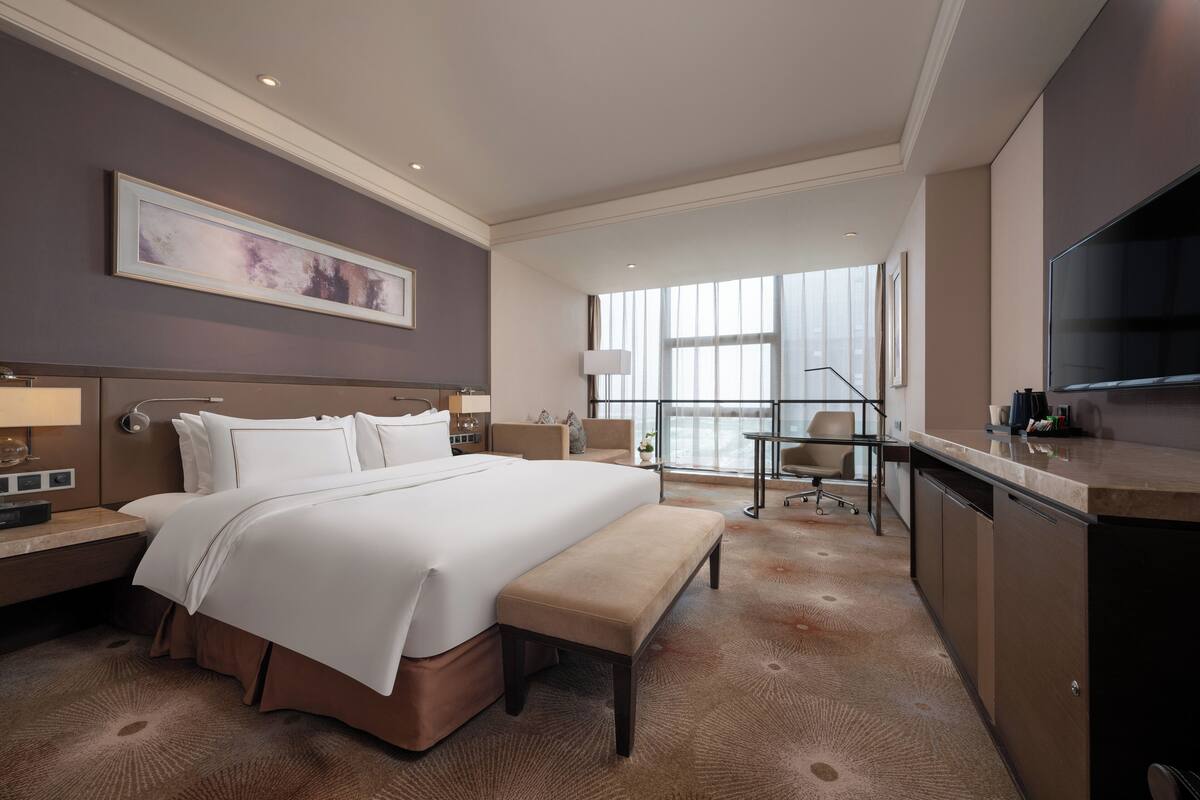 A hotel room with a large bed, a desk, a chair, and a TV.