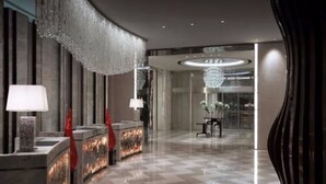 Um lobby de hotel moderno, com balcão de check-in, luminária de cristal e mesa de recepção.