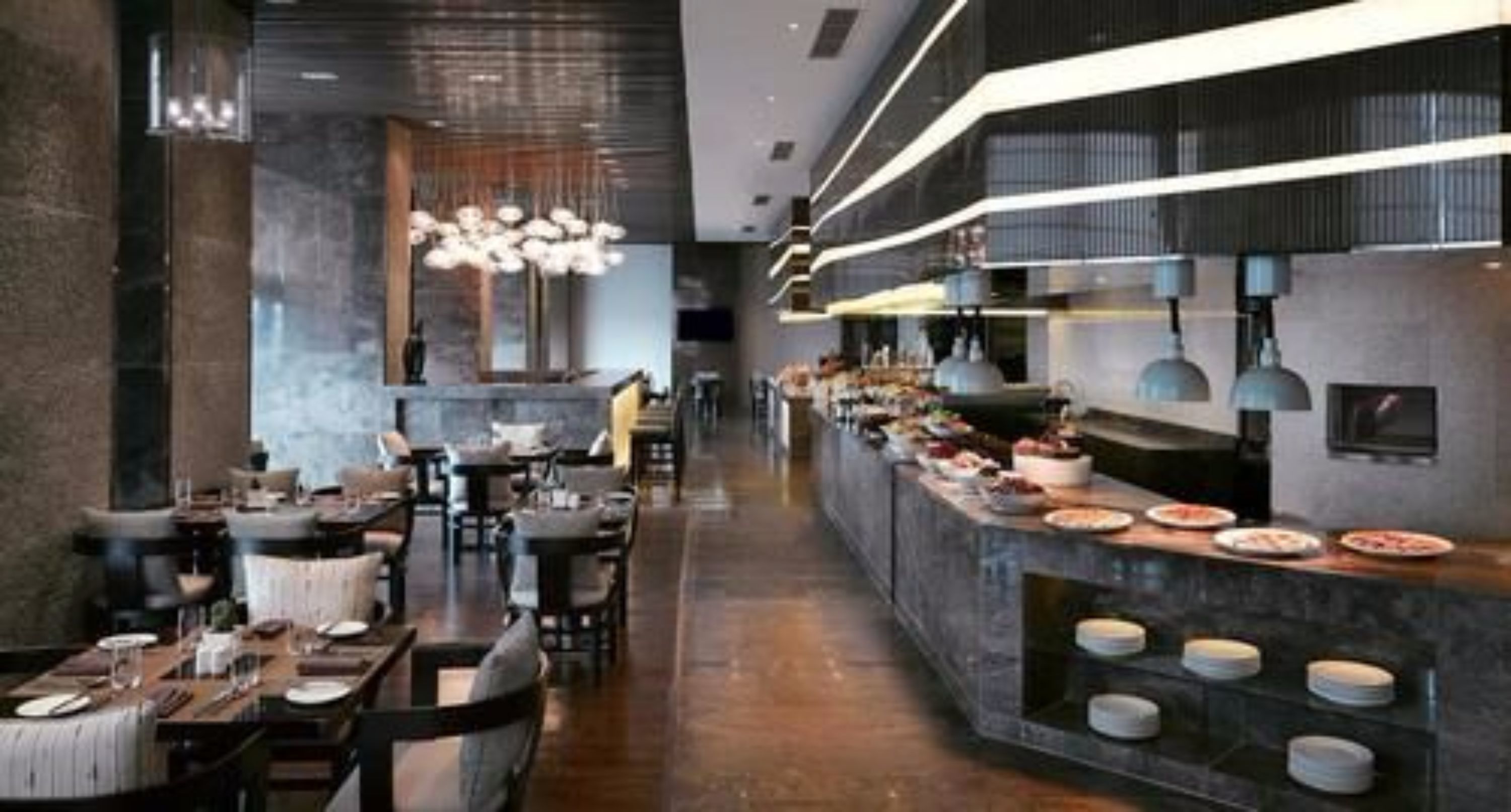 A modern restaurant with a long counter, multiple tables, and a variety of dishes displayed.