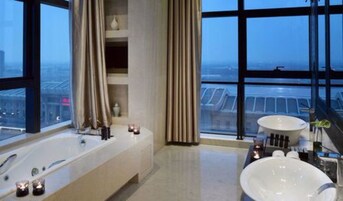 A modern bathroom with a large bathtub, a separate sink, and a view of the cityscape through large windows.