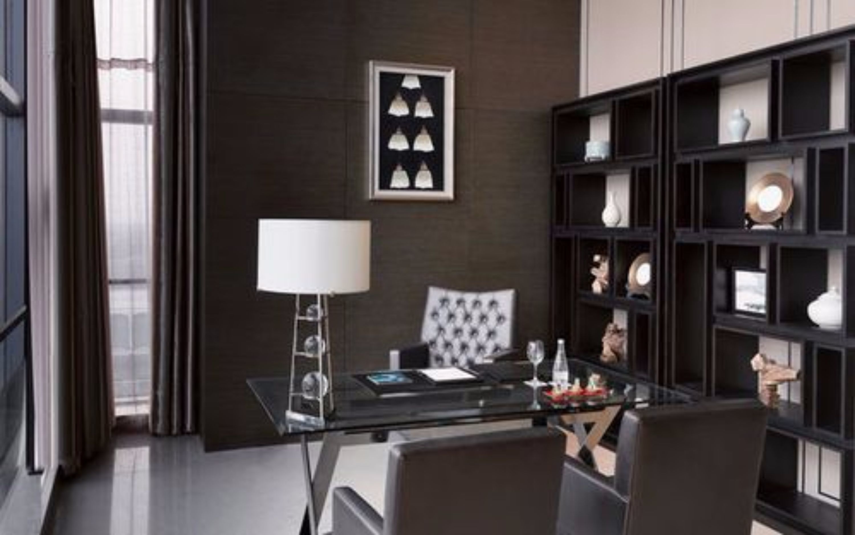 Una habitación moderna con una mesa de vidrio, una lámpara, una silla y un estante negro con objetos decorativos.