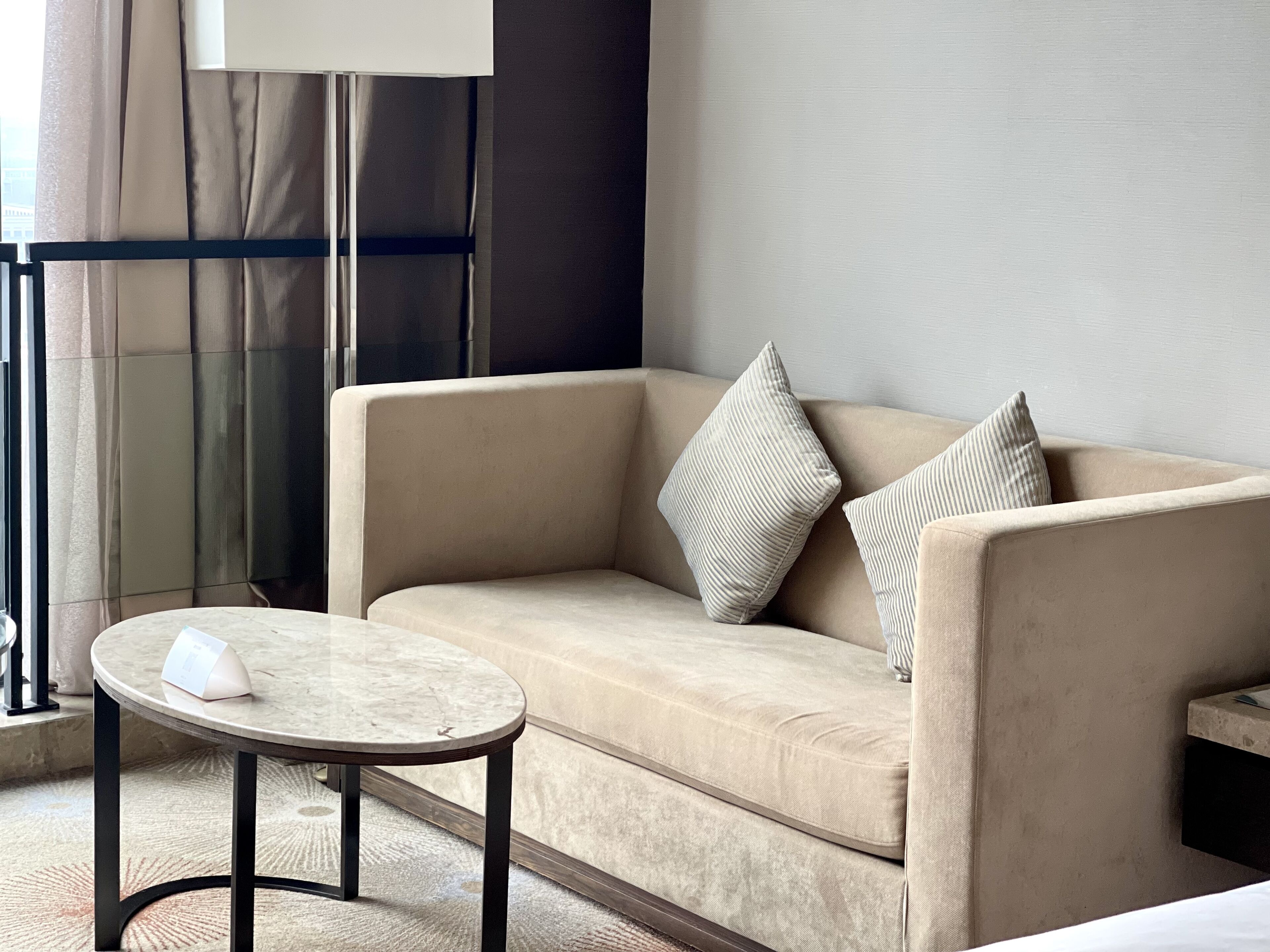 A beige sofa with two pillows, a small round table with a white object on it, and a floor lamp.