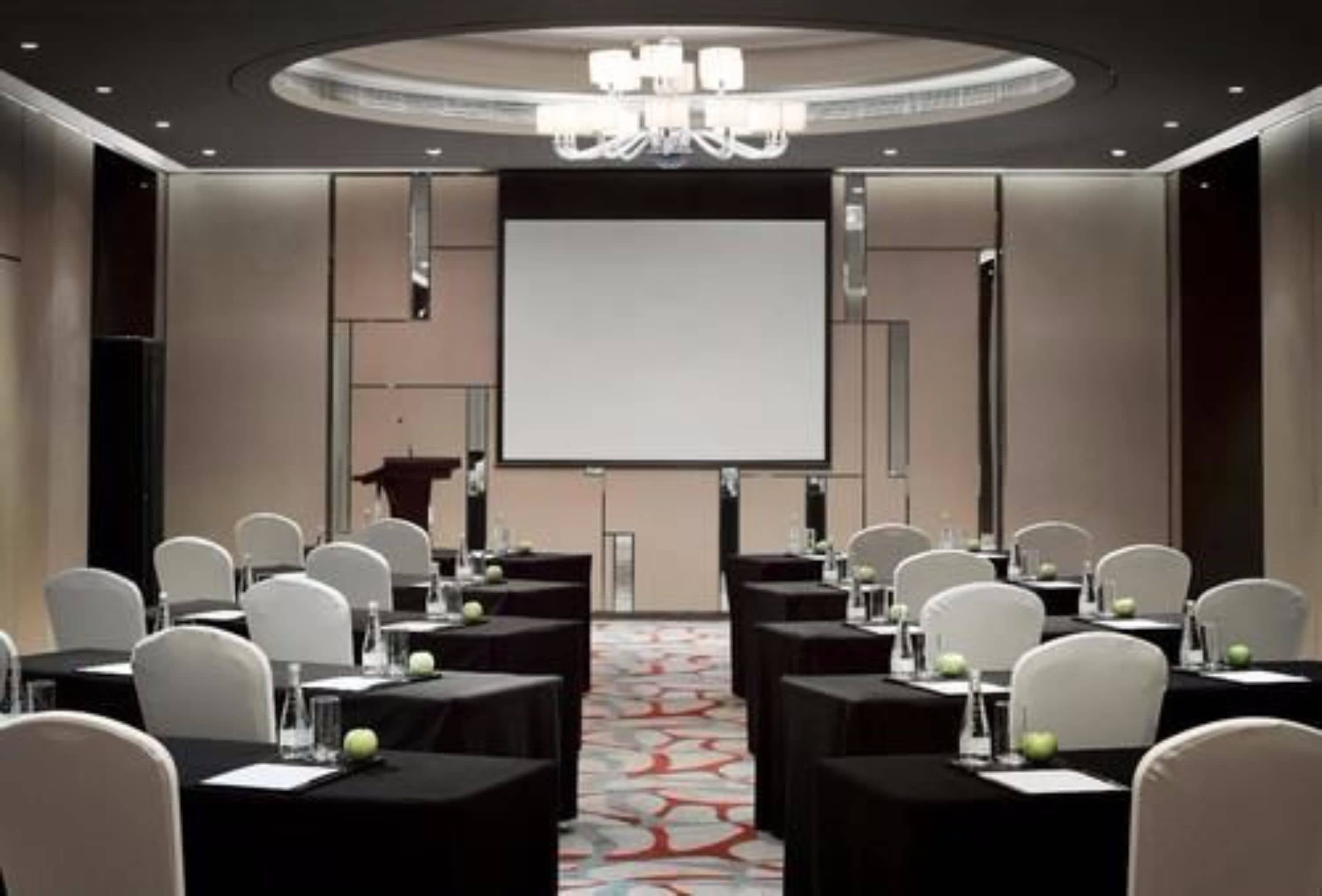 A conference room with a large screen, white chairs, and tables set up for a meeting.