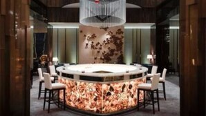 Um hall de hotel moderno com um bar circular central, um grande lustre e uma instalação de arte única na parede.
