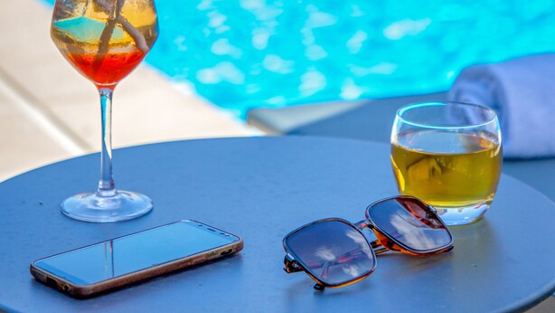 A table with a smartphone, sunglasses, and a drink near a pool.