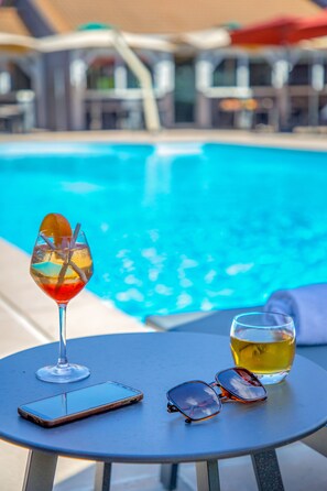 Una mesa con un teléfono inteligente, gafas de sol y una bebida cerca de una piscina.