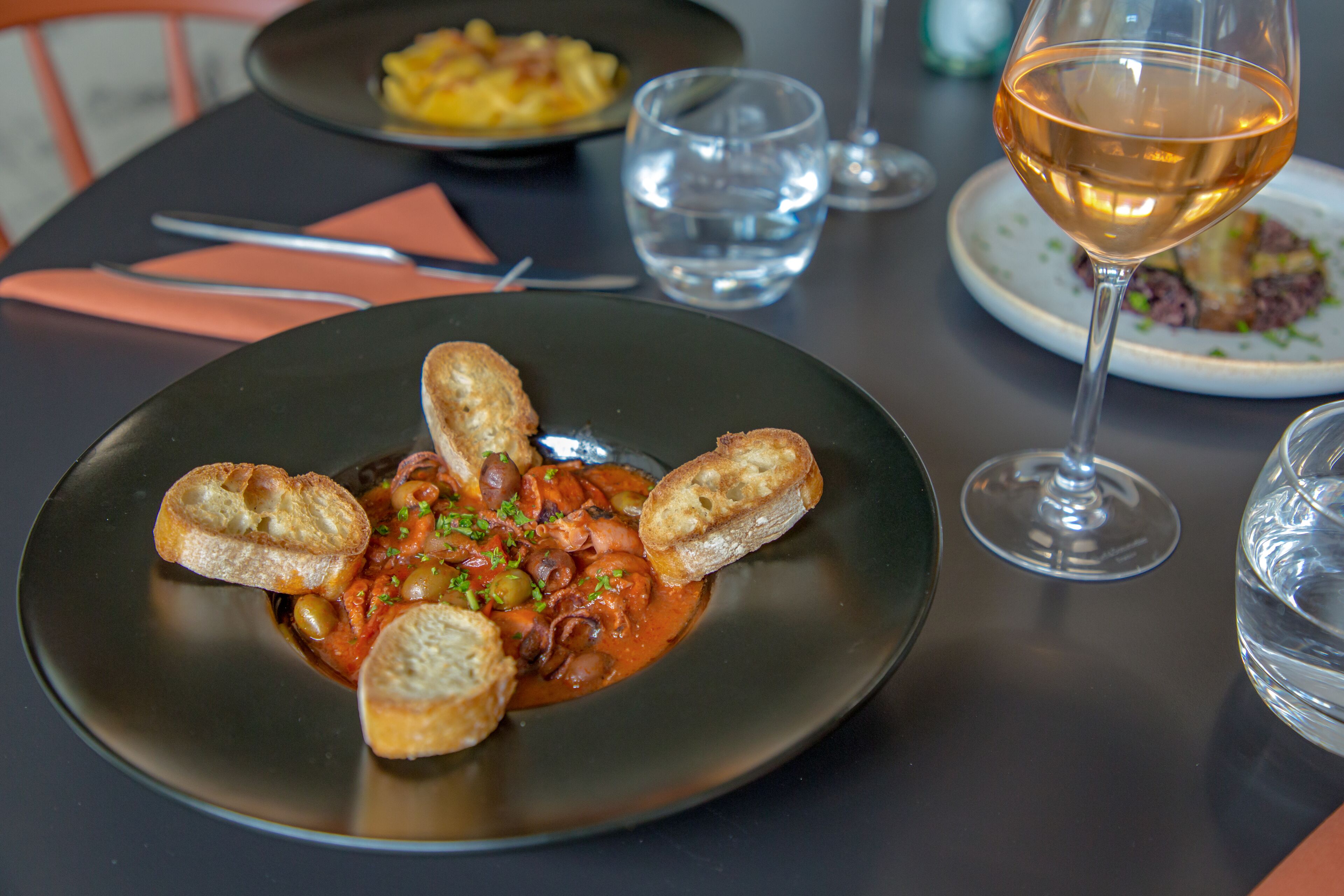 A dining table with a plate of food, a glass of wine, and a water glass.