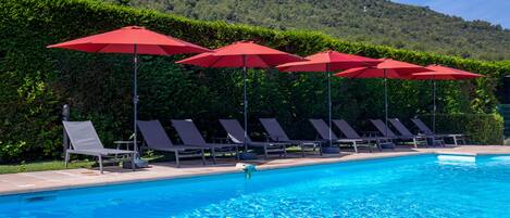 A swimming pool with red umbrellas and lounge chairs.