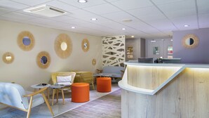 A modern reception area with a wooden reception desk, round wall mirrors, and a seating area with orange ottomans and light-colored chairs.