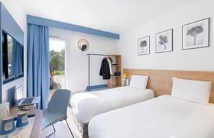 A hotel room with two beds, a desk with a laptop, a chair, and a wardrobe.