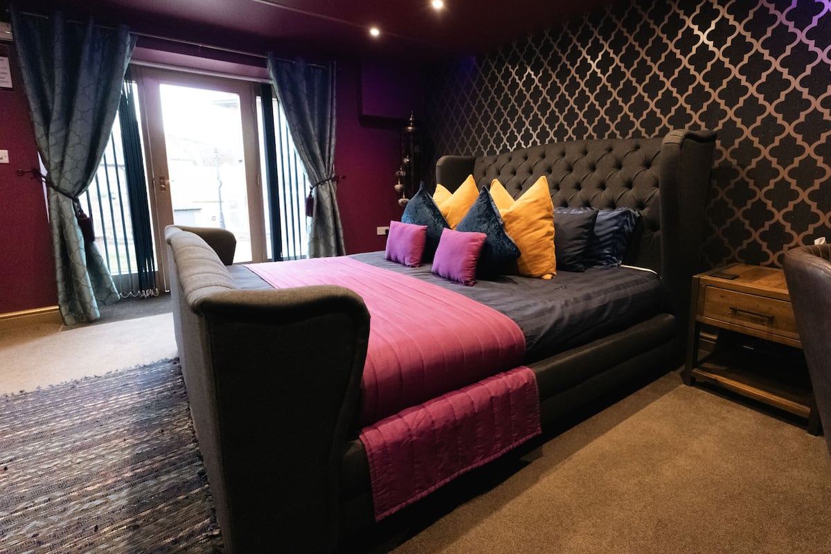 Un dormitorio con una cama grande, una mesita de noche, una silla y un papel tapiz estampado.