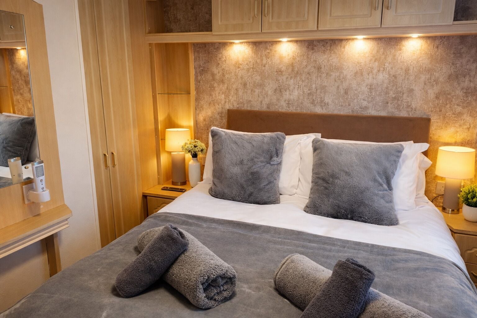 Habitación de hotel con cama, dos lámparas de noche, mesita de noche, espejo y un mueble de pared.