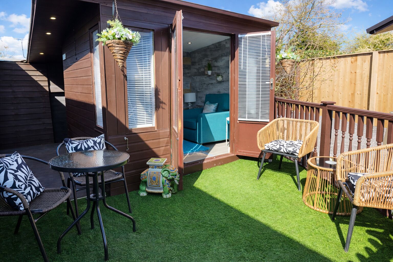 A wooden cabin with a patio area featuring a table, chairs, and a hanging plant.