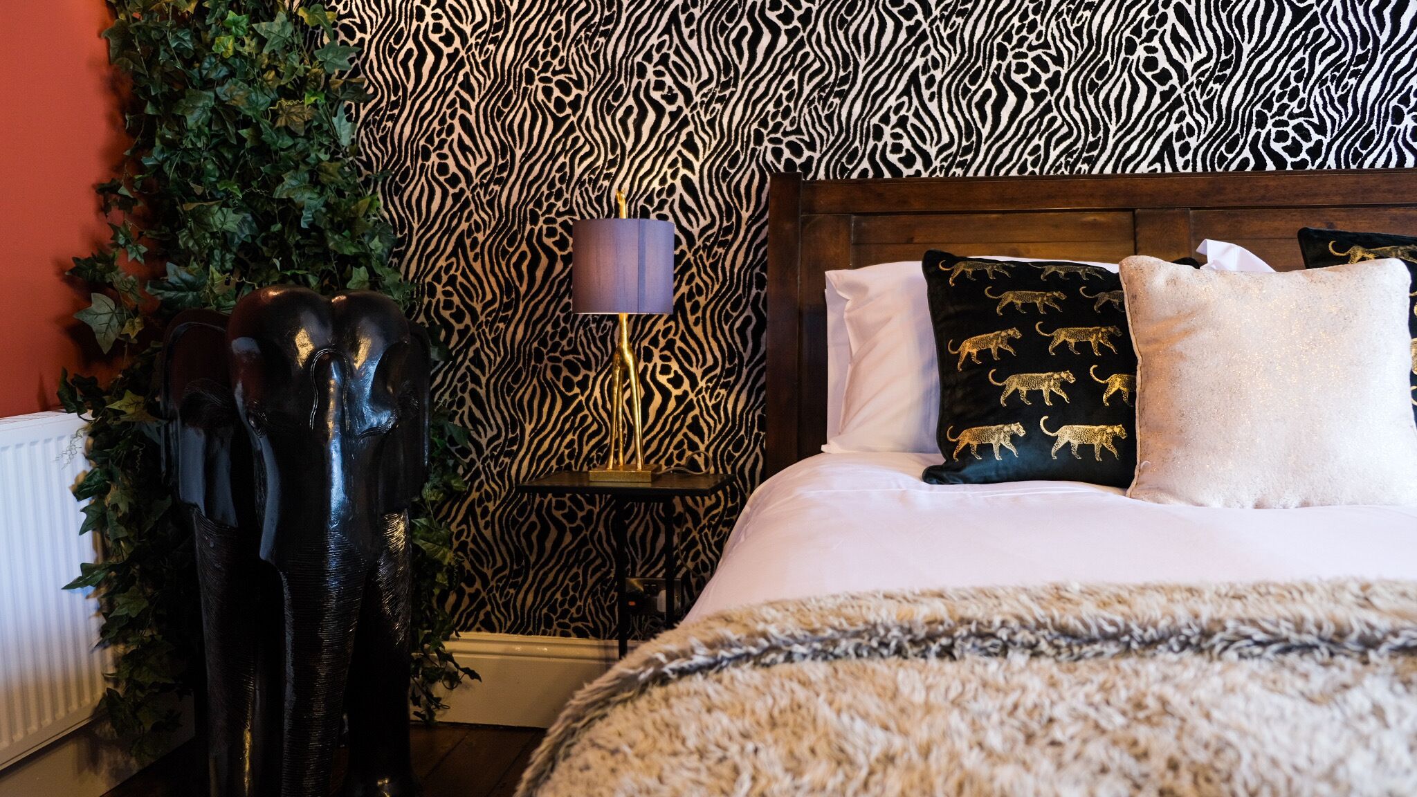 Une chambre à coucher avec une tête de lit à motifs zébrés, un lit avec des oreillers blancs et noirs, et une table de chevet avec une lampe.
