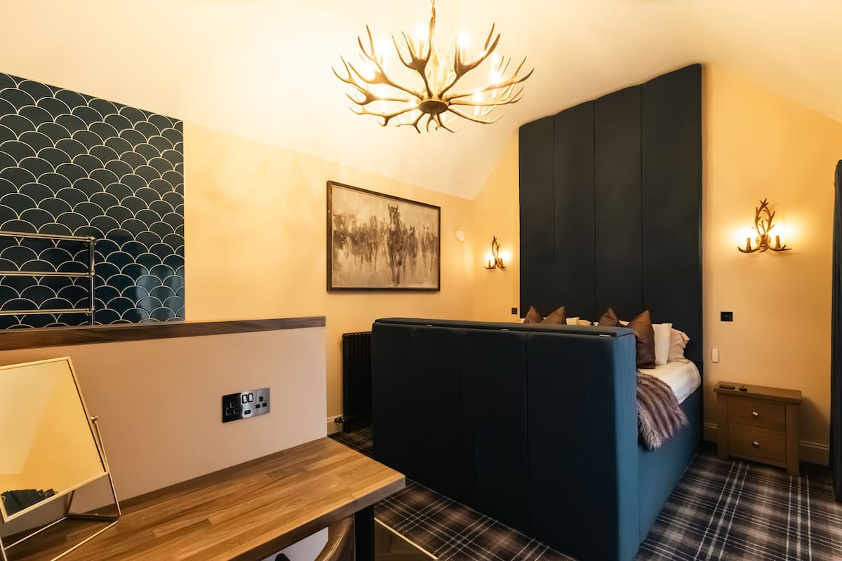 Habitación de hotel compacta con cama, una mesita, una silla, un cuadro colgado en la pared, un candelabro y un papel tapiz estampado.