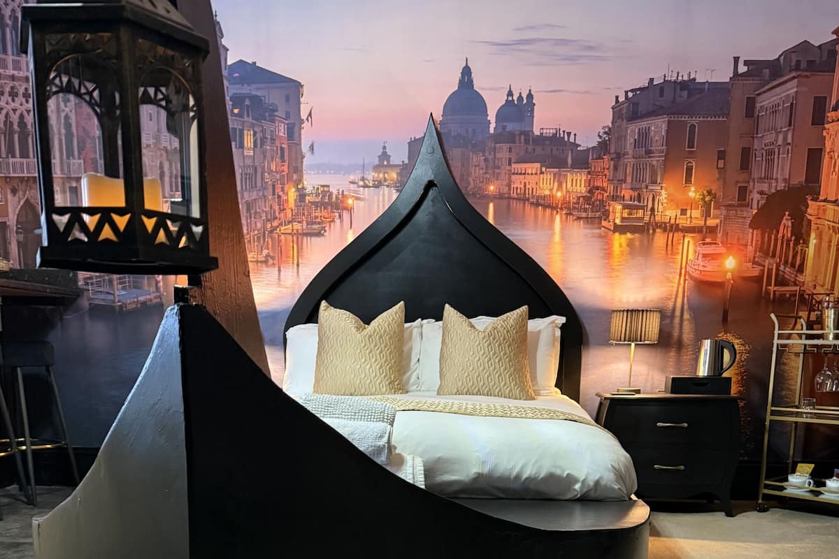 Una cama moderna con dosel negro en una habitación con vistas panorámicas a un paisaje urbano y un canal.