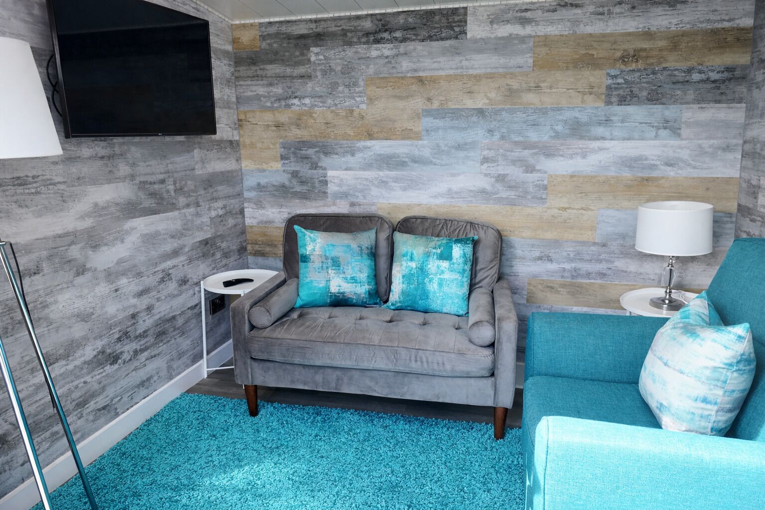 A room with a grey sofa, a teal armchair, and a blue carpet.