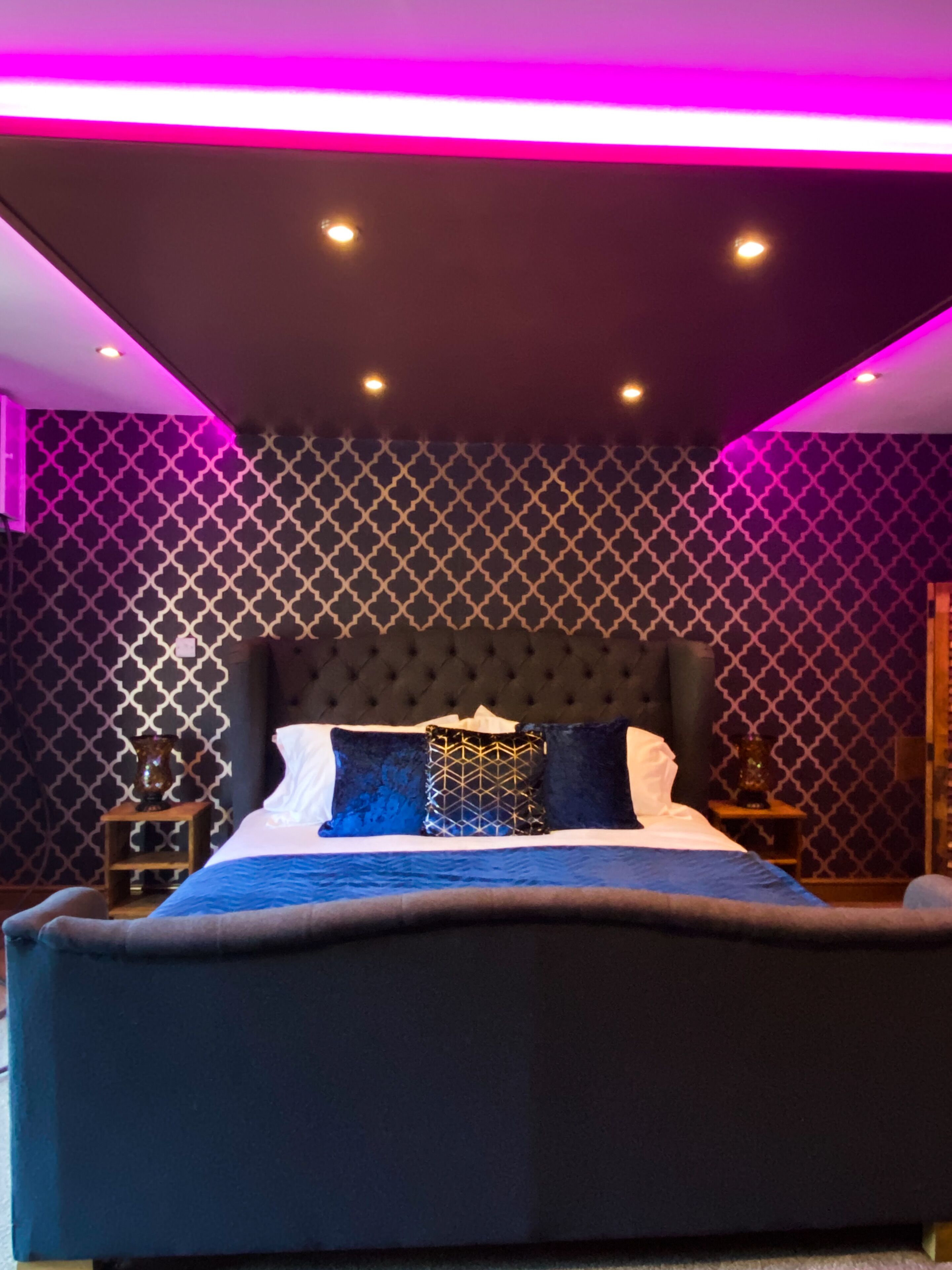 A modern bedroom with a tufted headboard, a patterned wall, and a bed with blue bedding.